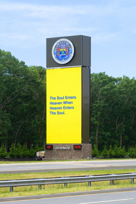 A digital billboard on the side of the road is yellow with blue text that reads 